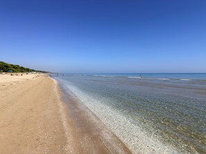 Uma praia com águas cristalinas, areal arenoso e alguns guarda-sóis.
