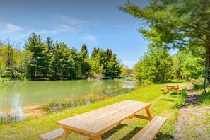 Ein Picknicktisch und eine Bank am Seeufer, im Hintergrund Bäume und ein Haus.
