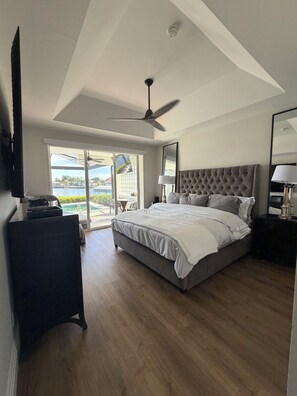 Ein Schlafzimmer mit einem großen Bett, einem Deckenventilator, einem Fernseher und Blick ins Freie.