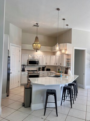 Eine moderne Küche mit weißen Schränken, einer großen Kochinsel mit Barhocker und Pendelleuchten.