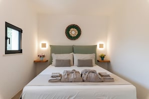 A neatly made bed with pillows and towels, a wall-mounted decorative plate, and bedside tables with lamps. - Luxury Trulli Zaccano Estate with Private Pool, Cisternino (Puglia)