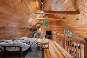 A cozy attic bedroom with a bed, desk, and seating area, featuring wooden walls and a stone accent wall. - Hot Tub • Game Room • 3 King Beds • Pet Friendly (Ellijay)