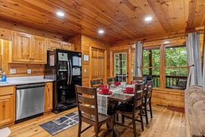 A cabin interior with a dining area, kitchen, and a large window. - Hot Tub • Game Room • 3 King Beds • Pet Friendly (Ellijay)