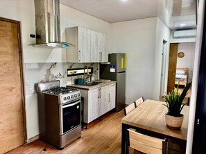 A compact kitchen with a gas stove, oven, and a built-in range hood. There is a dining table with chairs and a potted plant. - CasaMara #2, tropical bungalow in Private Residential area walkable to the beach (Las Terrenas)