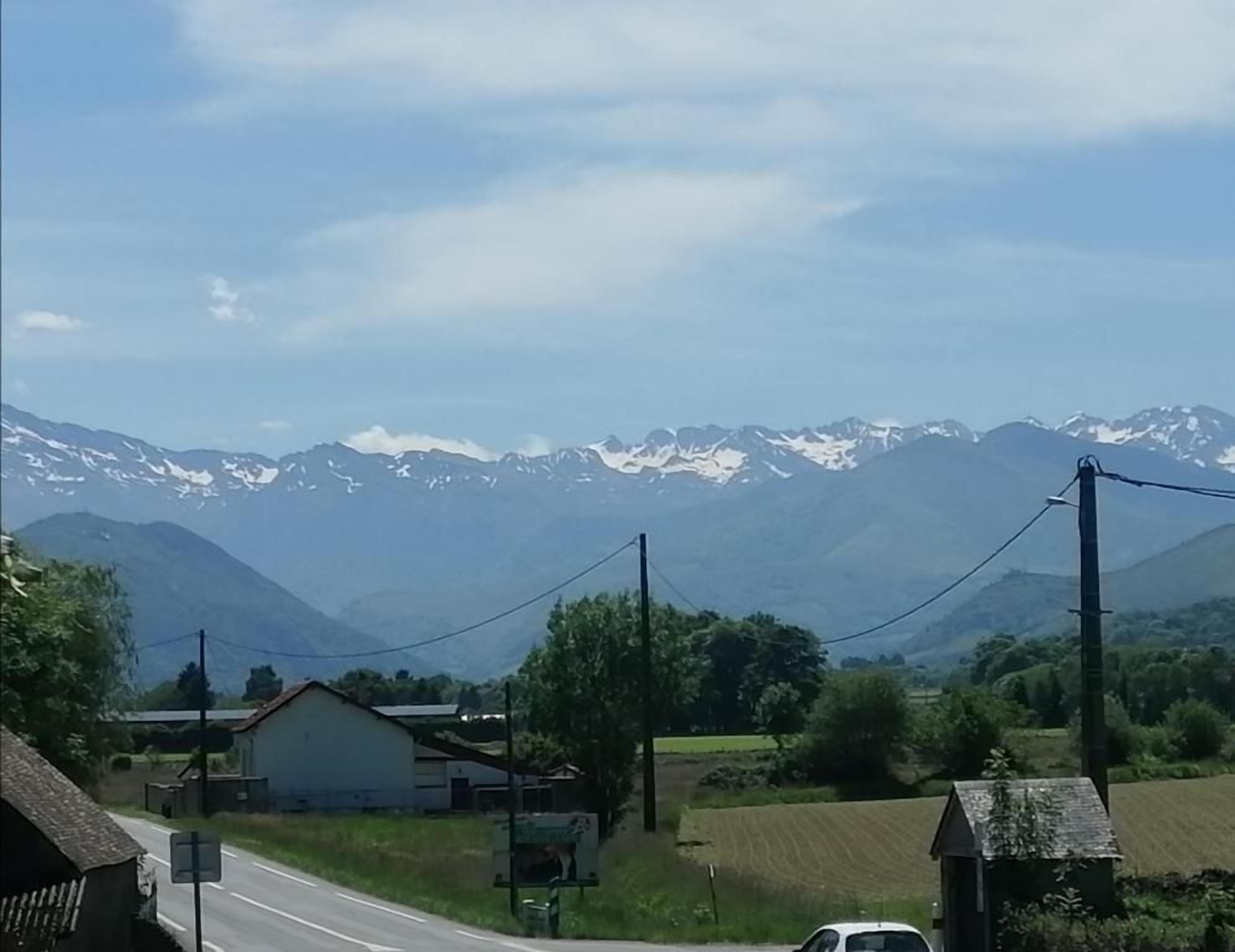 Une route de campagne bordée de maisons, avec une chaîne de montagnes en arrière-plan.