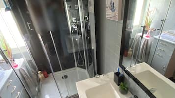 Une salle de bain moderne avec une douche à parois de verre, un grand miroir et un lavabo blanc.
