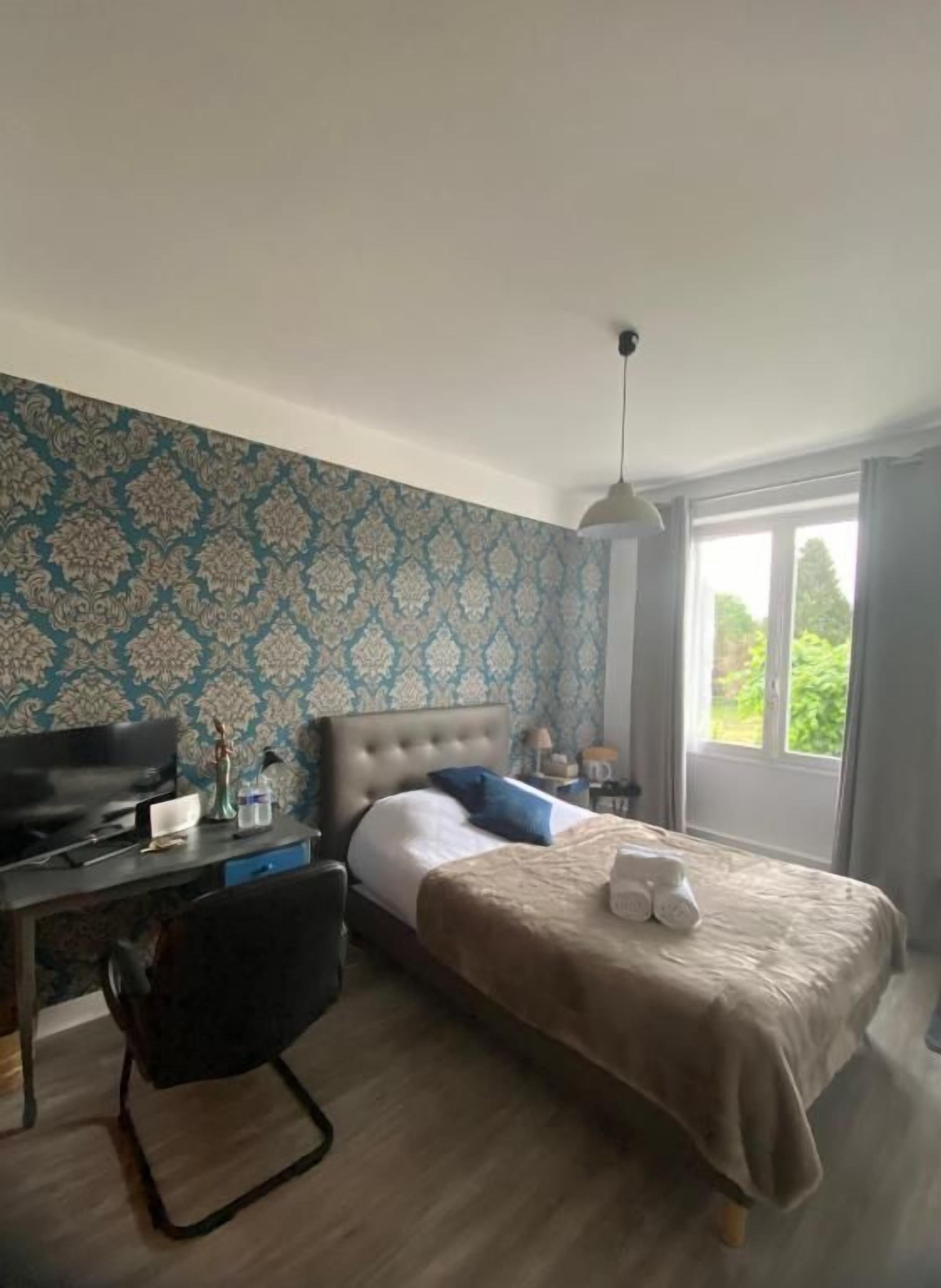 Een slaapkamer met een bed, een bureau, een stoel en een raam met uitzicht op groen.