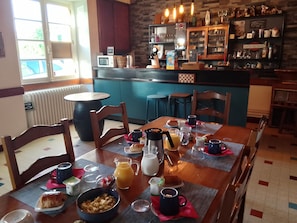 A breakfast setting with a table set for two, including a bowl of cereal, a croissant, a coffee mug, and a juice pitcher.