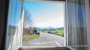 A window view of a road with a mountain range in the distance, a clear sky, and a rural landscape.