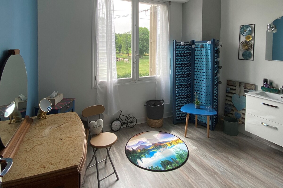 Una habitación con un ventanal grande, una mesa redonda con vistas panorámicas, una silla azul, una bicicleta pequeña y un armario blanco.