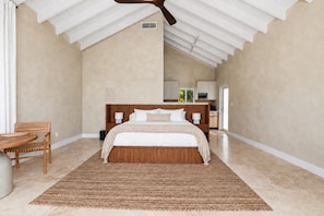 Un dormitorio con una cama grande, un cabecero de madera, una mesita de noche, una silla y un ventilador de techo.