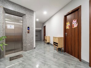 Un couloir moderne avec un sol en marbre, un ascenseur, des portes en bois et un petit meuble en bois.