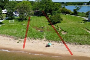 Een woonhuis met een groot gazon, een tennisbaan en een strandgedeelte.