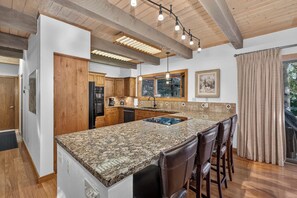 A kitchen with wooden cabinets, a granite countertop, a built-in island with bar stools, and a large window with a view. - Spring Hill Hideaway Fireplace (Vail)