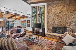 A spacious living room with a stone fireplace, leather sofas, and a large window offering a view of trees. - Spring Hill Hideaway Fireplace (Vail)