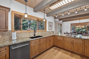 A kitchen with wooden cabinets, granite countertops, a dishwasher, and a window overlooking greenery. - Spring Hill Hideaway Fireplace (Vail)