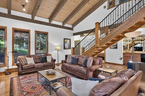 A spacious living room with leather sofas, a coffee table, and a large window overlooking a garden. - Spring Hill Hideaway Fireplace (Vail)