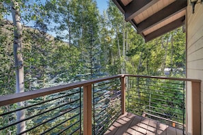 A wooden deck with a metal railing overlooking a forested area. - Spring Hill Hideaway Fireplace (Vail)