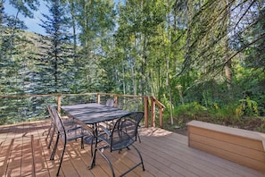 An outdoor deck with a table and chairs, surrounded by dense forest. - Spring Hill Hideaway Fireplace (Vail)