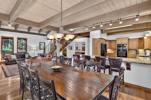 A spacious dining area with a large wooden table and chairs, a kitchen with wooden cabinets, and a staircase leading to an upper level. - Spring Hill Hideaway Fireplace (Vail)