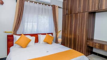 A hotel room with a bed, curtains, a wardrobe, and a bedside table.