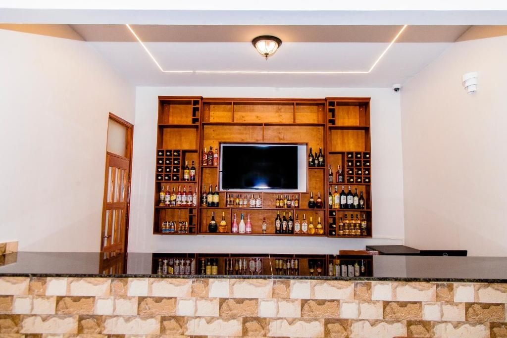 Una zona de bar con un televisor de pantalla plana, estantes de madera con botellas y una pared de piedra.