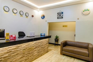 A reception area with a reception desk, a laptop, a clock, a sofa, and a welcome sign. - Belmont Hotel Mbale (Mbale)