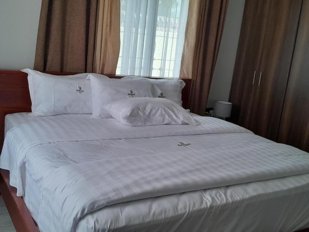 Una cama bien hecha con ropa blanca y almohadas, un cabecero de madera y una ventana con cortinas.