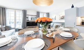 A modern dining area with a wooden table set for a meal, a vase of flowers, and a kitchen in the background. - CENTRAL PARIS LUXURY APARTMENT WITH HIGH-END AMENITIES (Paris)