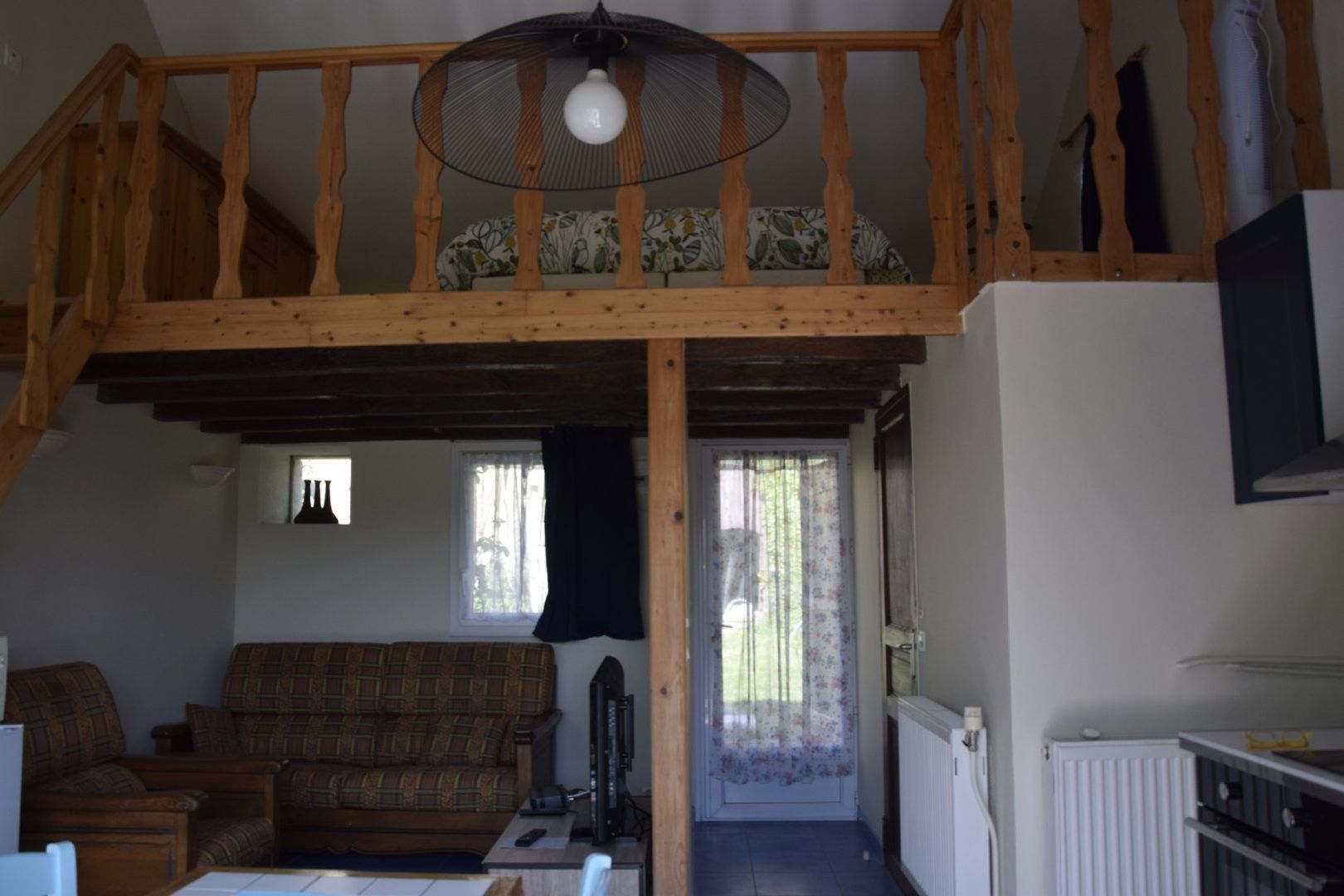 Een loft-achtige woonruimte met een houten trap, een bank, een televisie en een deur naar een buitenruimte.