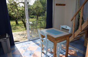 A room with a table and chairs, a wooden staircase, and a view of a garden through a glass door.