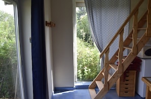 A wooden staircase leading to a balcony with a view of greenery outside.