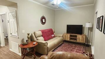 A living room with a sofa, a television, a ceiling fan, and a decorative wall hanging.