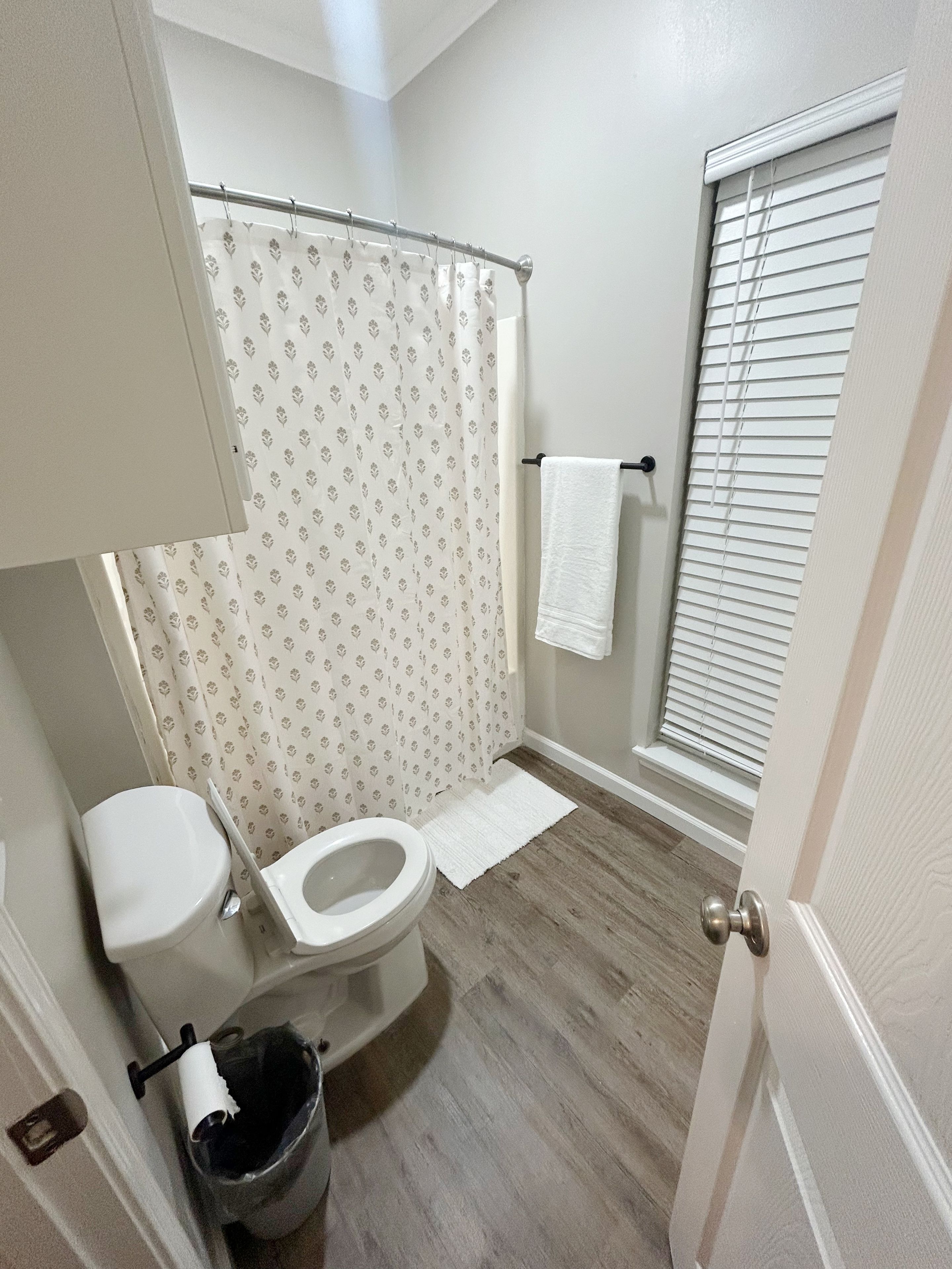 Un baño con inodoro, cortina de ducha, toallero y una ventana con persianas.