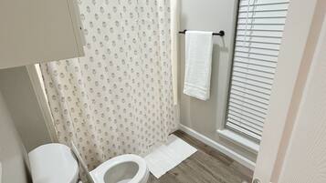 Un baño con inodoro, cortina de ducha, toallero y una ventana con persianas.