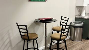 A small dining area with a round table and two chairs, a trash can, and a kitchen counter with cabinets.