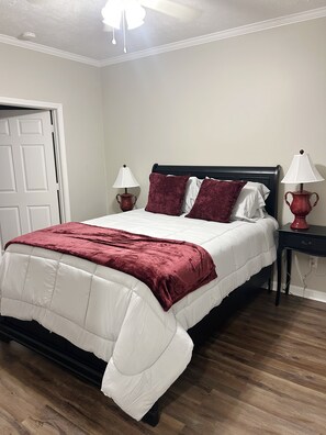 Un dormitorio con una cama, dos mesitas de noche, una puerta y un ventilador de techo.
