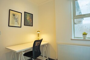 A room with a white desk, a black chair, a lamp, and two framed pictures on the wall. - Crwys Road 4-Bed Apartment, Near City Centre, Great for Long Stays (Cardiff)