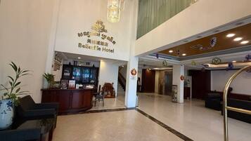 Un hall de hotel con mostrador de recepción, zona de estar y escalera que lleva a plantas superiores.