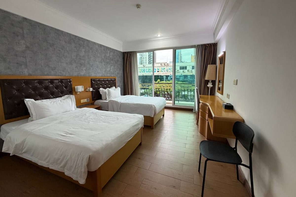 A hotel room with two beds, a desk, a chair, and a large window with a view.