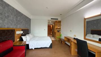 Una habitación de hotel con una cama, un escritorio, una silla, un sofá rojo y un espejo.