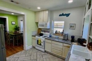 Una cocina equipada con microondas, estufa y lavaplatos. Hay una zona de comedor con sillas y una mesa. Las paredes están pintadas de verde, y hay un letrero en la pared.