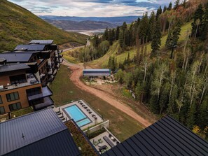 Ein modernes Hotel mit Schwimmbad, mehreren Balkonen und Blick auf eine Berglandschaft.