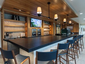 A bar area with a long counter, multiple bar stools, and a television screen mounted on the wall. - PARQ Founders Place Ski In-Out Pool Fitness Yoga Sauna Game Room Private Hot Tub (Park City)