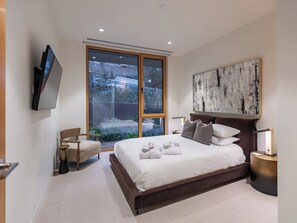 A modern bedroom with a large bed, a TV mounted on the wall, and a view of the outdoors through a sliding glass door. - PARQ Founders Place Ski In-Out Pool Fitness Yoga Sauna Game Room Private Hot Tub (Park City)