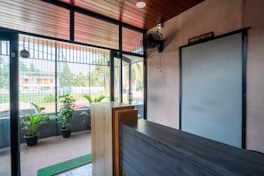 A reception area with a wooden reception desk, a check-out time sign, and potted plants. - Abrigo Rooms and Homes, Calicut (Kozhikode)