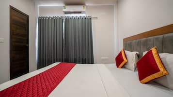 A hotel room with a bed, a headboard, a window with curtains, and an air conditioning unit.
