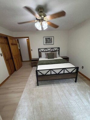 A bedroom with a bed, nightstands, a ceiling fan, and a door. - Peaceful Moultonborough Getaway | Sleeps 14 (Moultonborough)