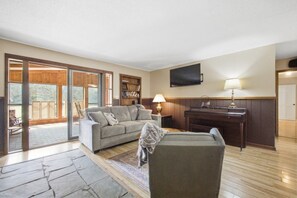 A spacious living area with a sofa, a chair, a piano, and a television on the wall. - Retreat at Delano | Near Hiwassee & Scenic Railway (Delano)