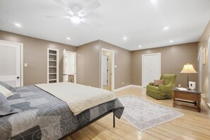 Ein Schlafzimmer mit einem Bett, einem grünen Sessel, einem Nachttisch, einem Deckenventilator und einem begehbaren Kleiderschrank.